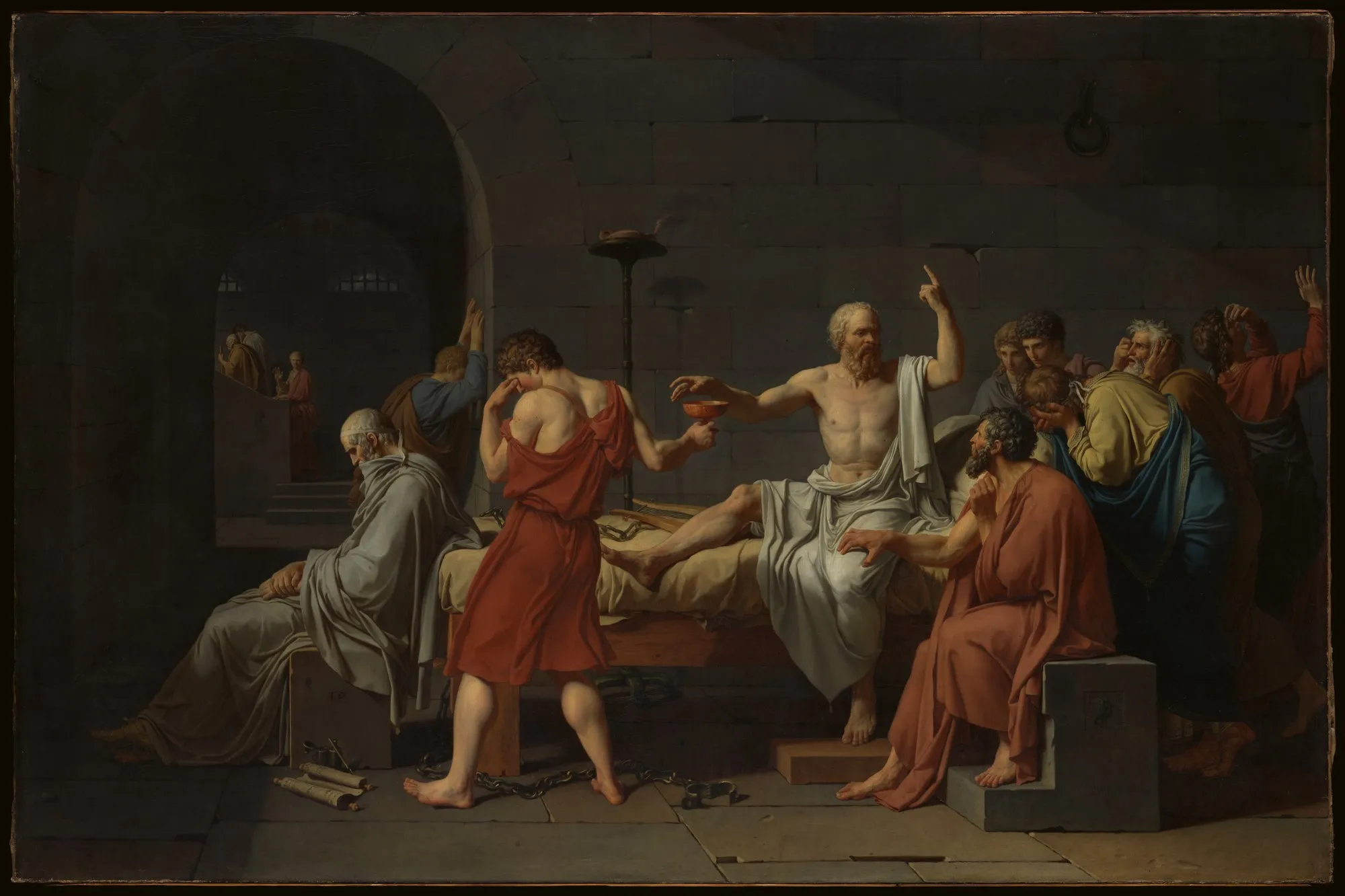 An oil painting of Socrates in a stone prison cell: white-haired and bare-chested, he sits up on his bed with one finger raised, reaching for a cup of hemlock that a young man in red holds out with his face turned away, while grieving followers crowd around.