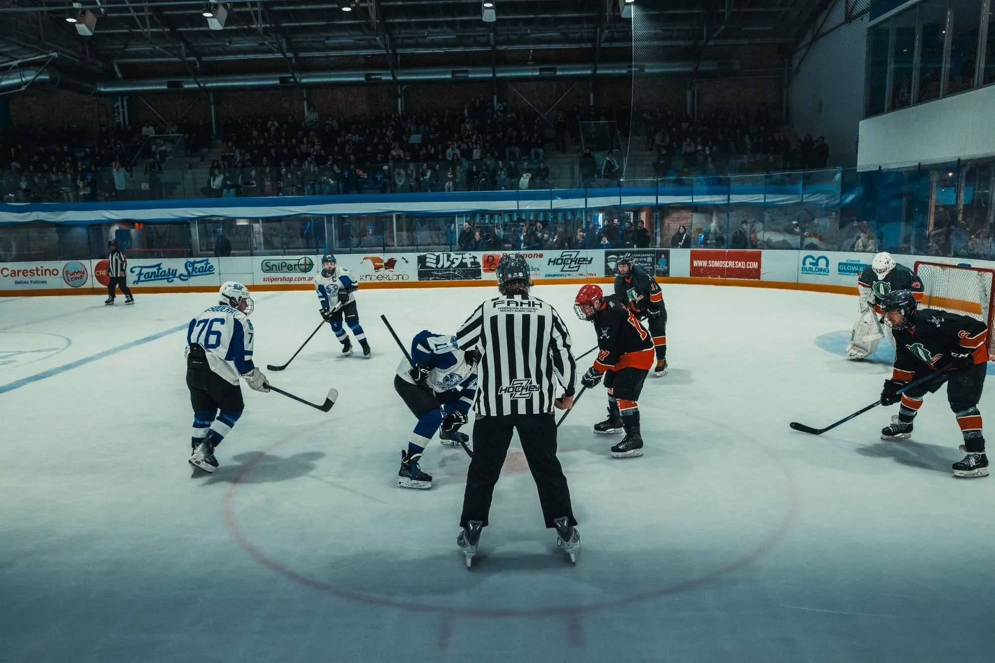 An ice hockey face-off in a packed indoor arena in Buenos Aires, with players from both teams in action.