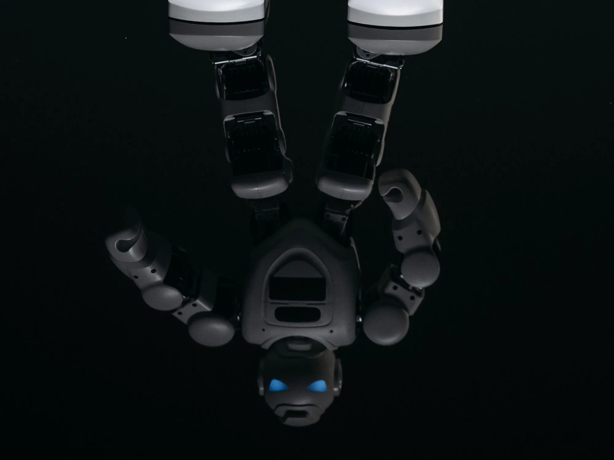 A white toy robot's feet stand at the top edge of a glossy black surface, and below them its reflection hangs upside down in shadow, blue eyes glowing near the bottom.